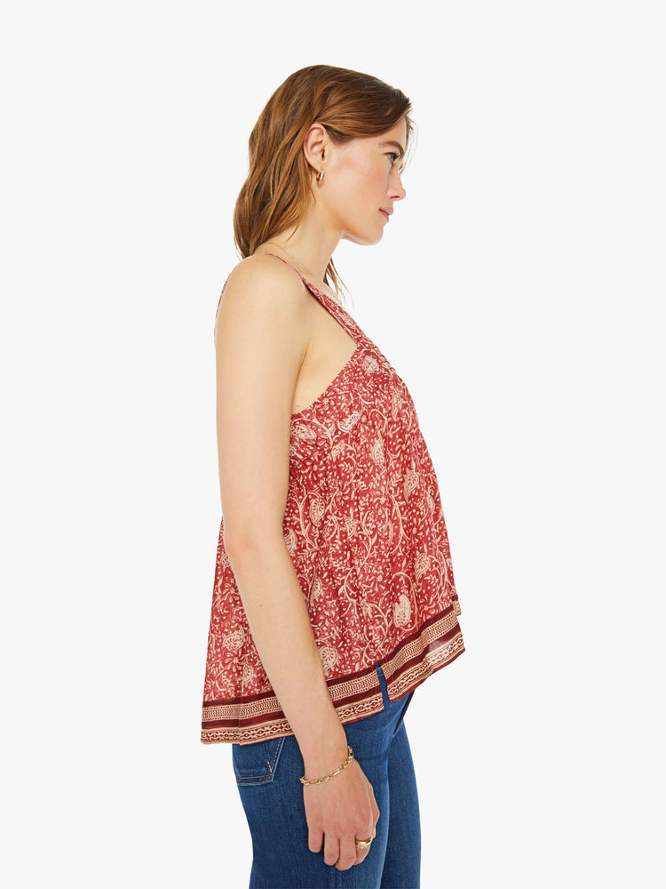 Side view of a woman in a in terracotta with a warm-toned floral print and stripes at the hem, and features detailed straps and buttons in the back.