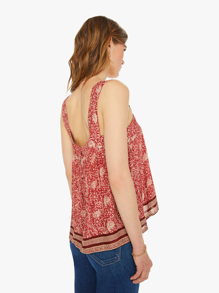 Back view of a woman in a in terracotta with a warm-toned floral print and stripes at the hem, and features detailed straps and buttons in the back.