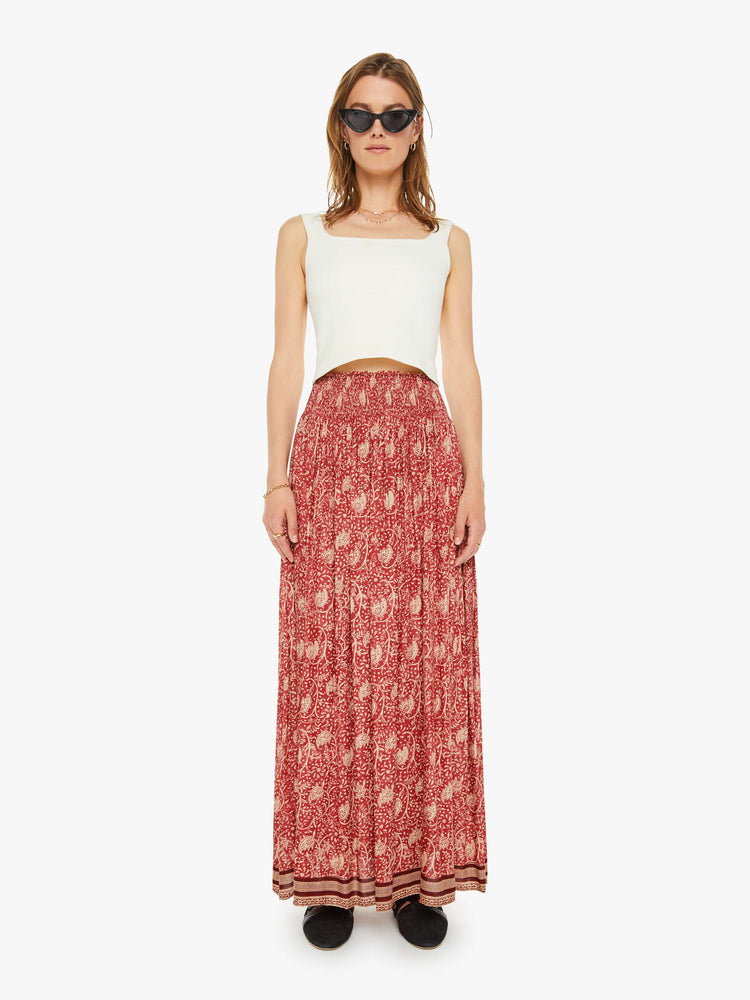 Front view of a woman in a maxi skirt  floral print and stripes at the hem, the skirt has a smocked waistband and a loose, flowy fit. 