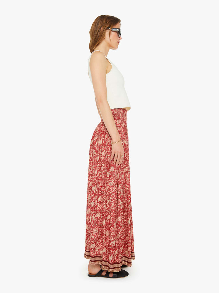 Side view of a woman in a maxi skirt  floral print and stripes at the hem, the skirt has a smocked waistband and a loose, flowy fit. 