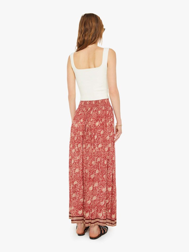 Back view of a woman in a maxi skirt  floral print and stripes at the hem, the skirt has a smocked waistband and a loose, flowy fit. 