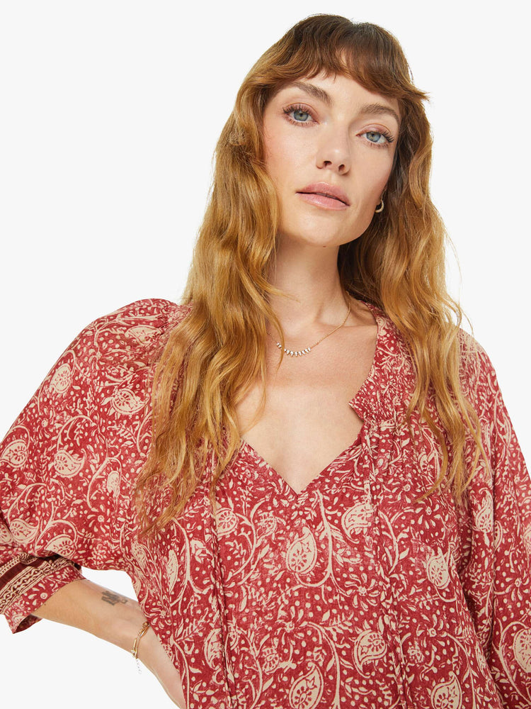 Close up view of a woman in a floral flowy mini dress with a keyhole neckline with a tasseled tie closure, 3/4-length sleeves and a wide ruffle at the hem.