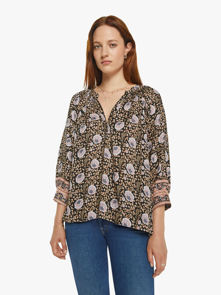 Front view of a woman in black floral print V-shaped neckline with covered buttons and subtle pleats below the collar emphasizes the loose, flowy feel top.