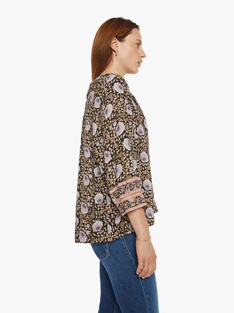 Side view of a woman in black floral print V-shaped neckline with covered buttons and subtle pleats below the collar emphasizes the loose, flowy feel top.