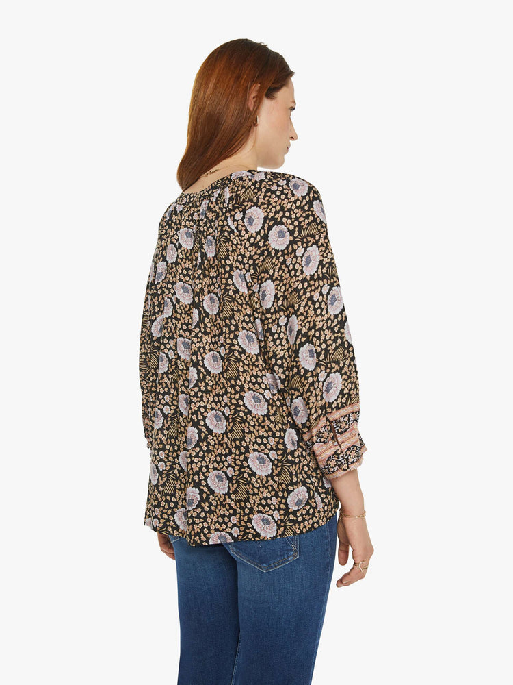 Back view of a woman in black floral print V-shaped neckline with covered buttons and subtle pleats below the collar emphasizes the loose, flowy feel top.