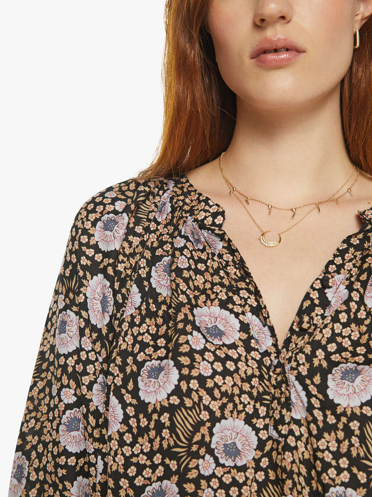 Close up view of a woman in black floral print V-shaped neckline with covered buttons and subtle pleats below the collar emphasizes the loose, flowy feel top.