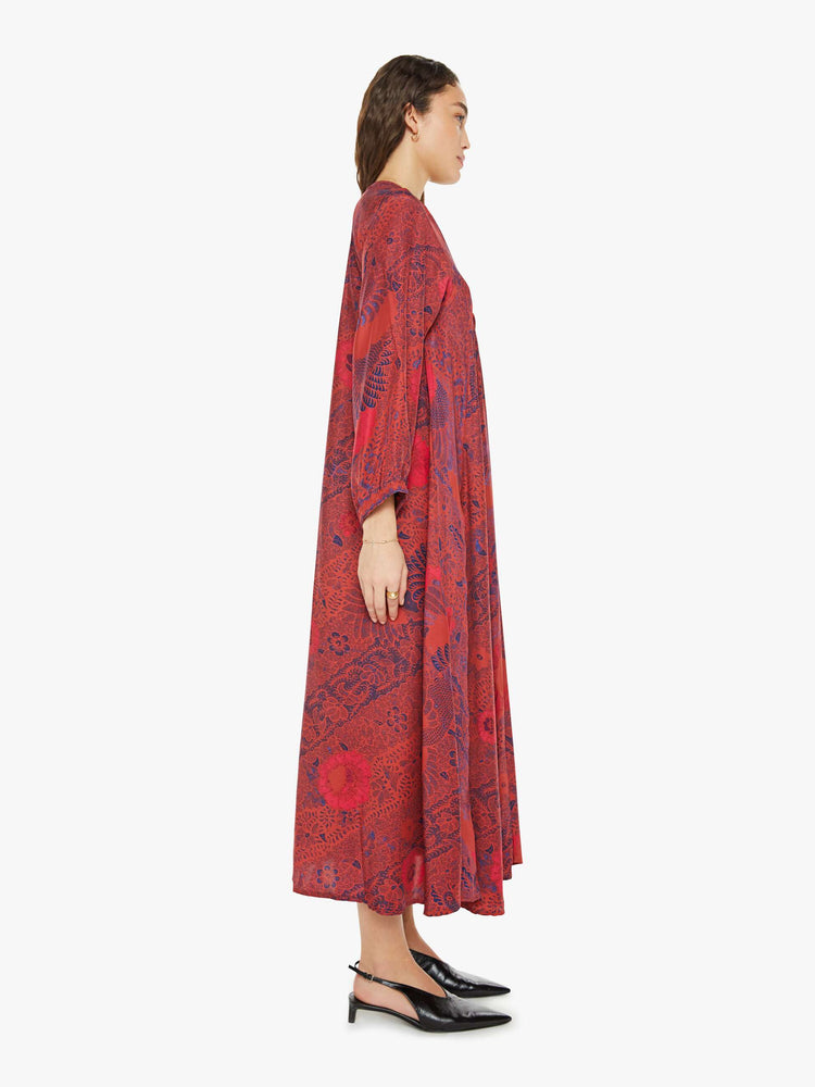 Side view of a woman in a red with blue floral print maxi dress with voluminous sleeves and has an A-line cut for a loose, breezy feel.