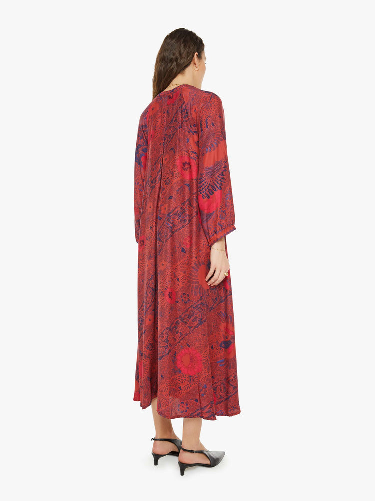 Back view of a woman in a red with blue floral print maxi dress with voluminous sleeves and has an A-line cut for a loose, breezy feel.