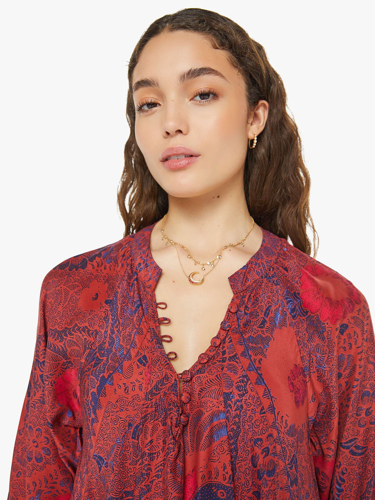 Close up view of a woman in a red with blue floral print maxi dress with voluminous sleeves and has an A-line cut for a loose, breezy feel.