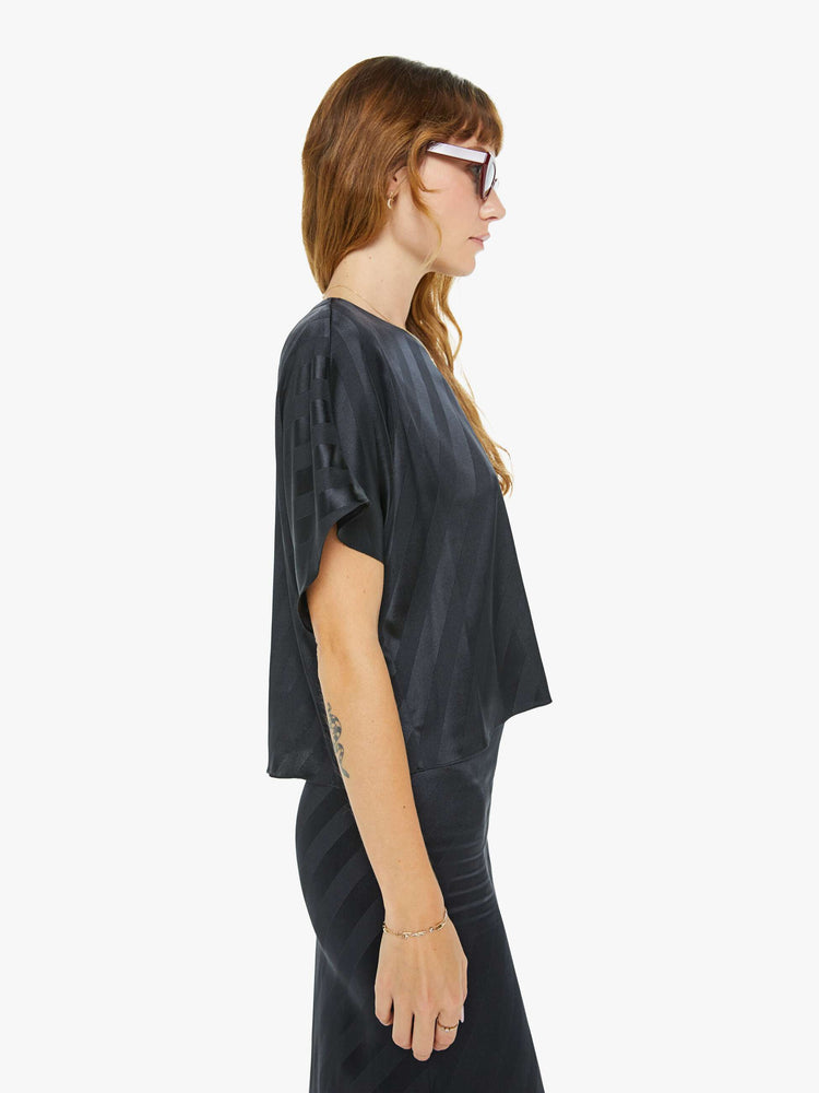 Side view of a woman in black with diagonal stripes with short dolman sleeves, a slightly cropped hem and a loose, flowy fit.