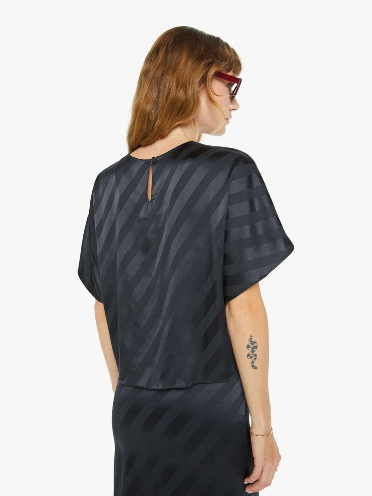 Back view of a woman in black with diagonal stripes with short dolman sleeves, a slightly cropped hem and a loose, flowy fit.