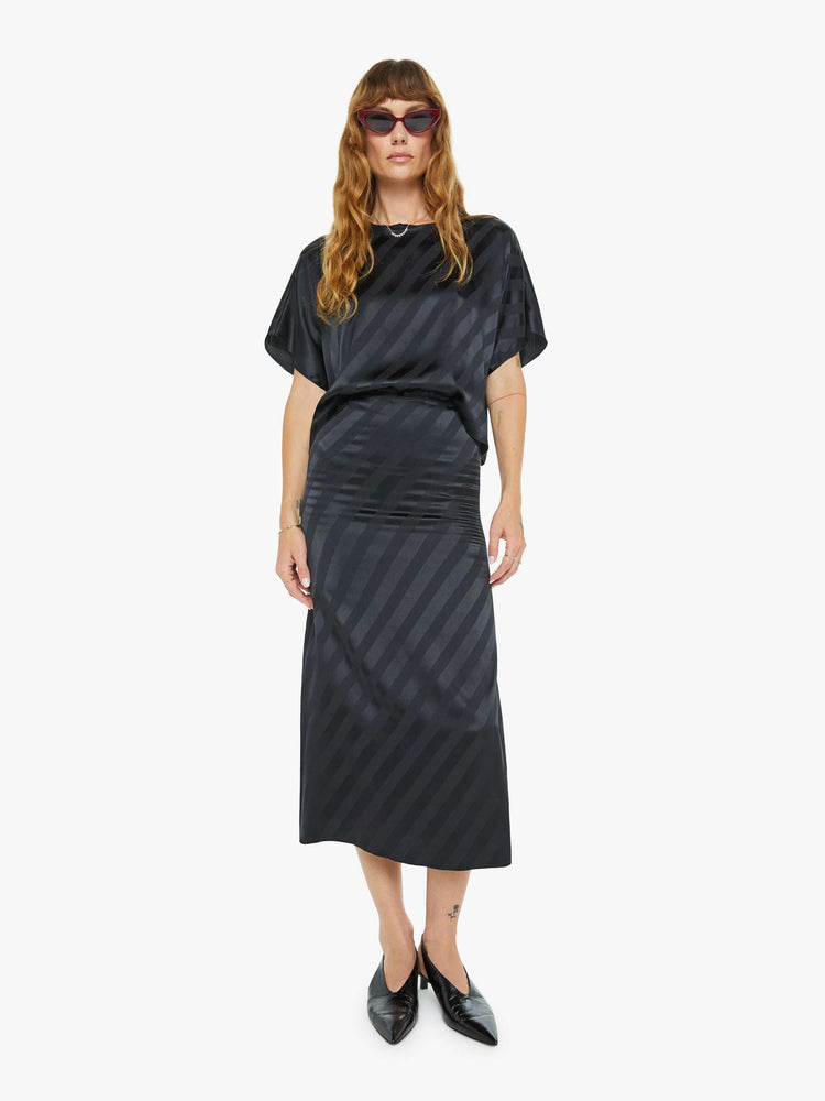 Front view of a woman in a black with diagonal stripes bias cut maxi skirt with a straight fit and ankle- grazing hem.