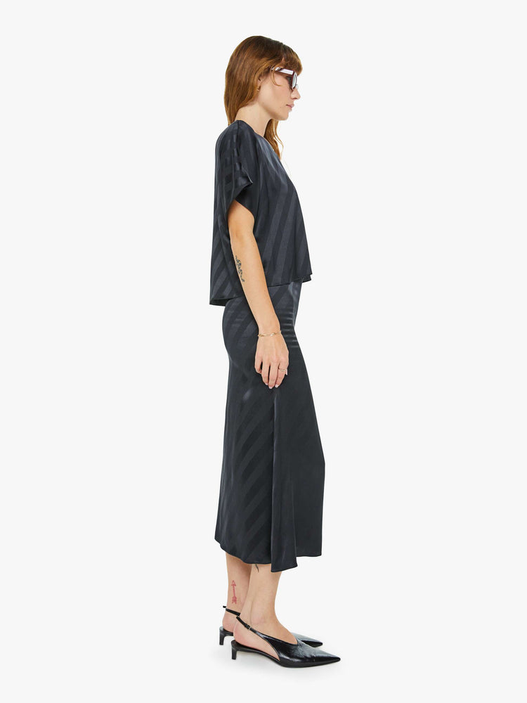 Side view of a woman in a black with diagonal stripes bias cut maxi skirt with a straight fit and ankle- grazing hem.