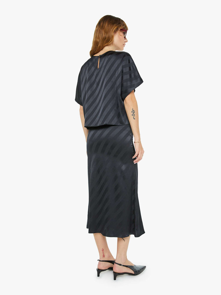 Back view of a woman in a black with diagonal stripes bias cut maxi skirt with a straight fit and ankle- grazing hem.