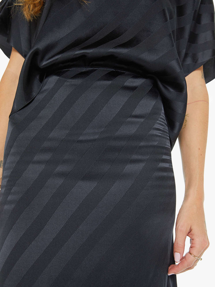 Close up view of a woman in a black with diagonal stripes bias cut maxi skirt with a straight fit and ankle- grazing hem.