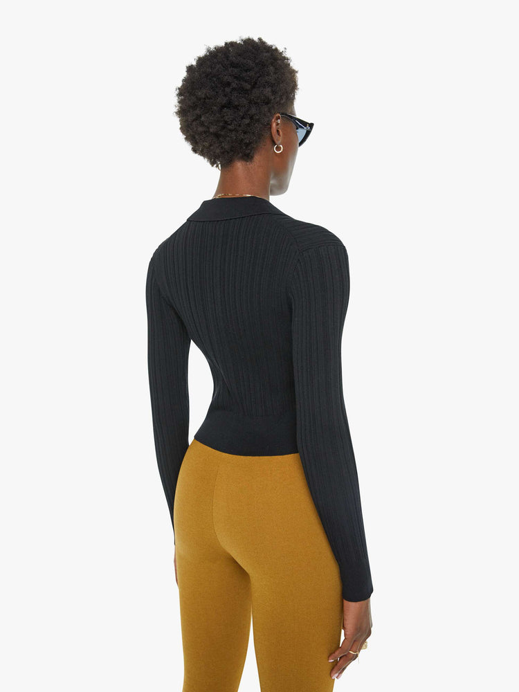 Back view of a woman in a black top with a collar, buttoned V-neck, long sleeves and a cropped fit.