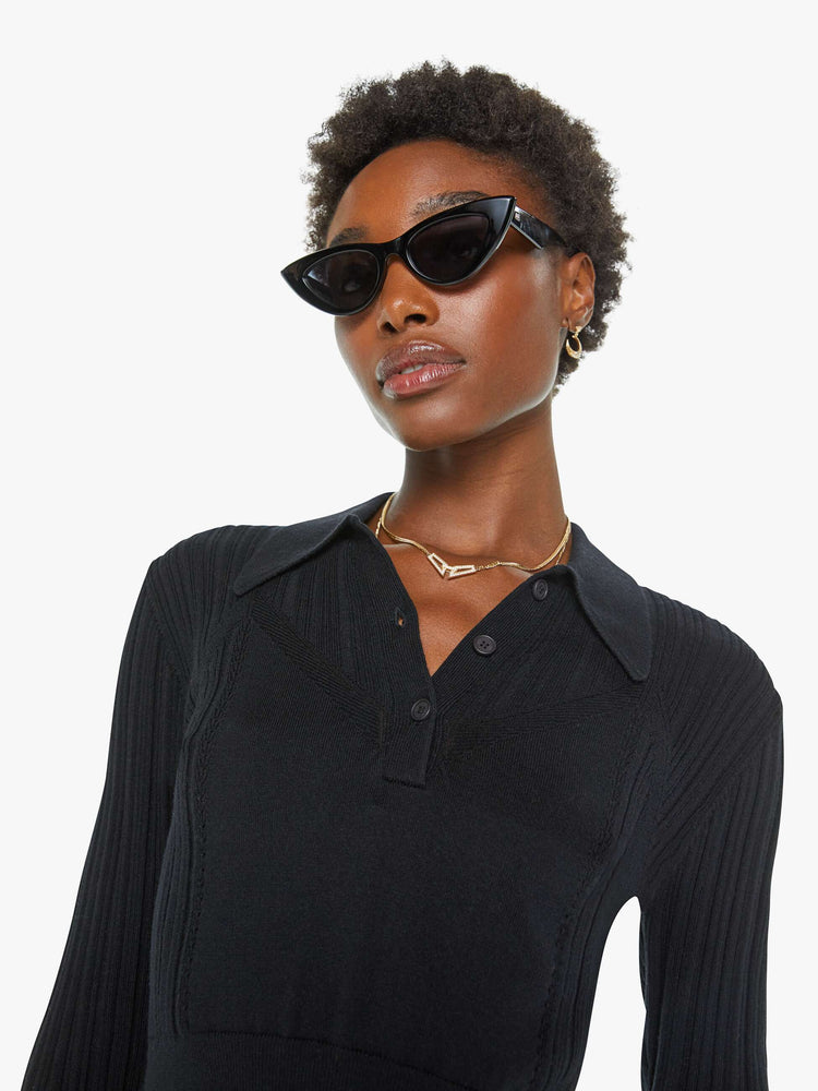 Close up view of a woman in a black top with a collar, buttoned V-neck, long sleeves and a cropped fit.