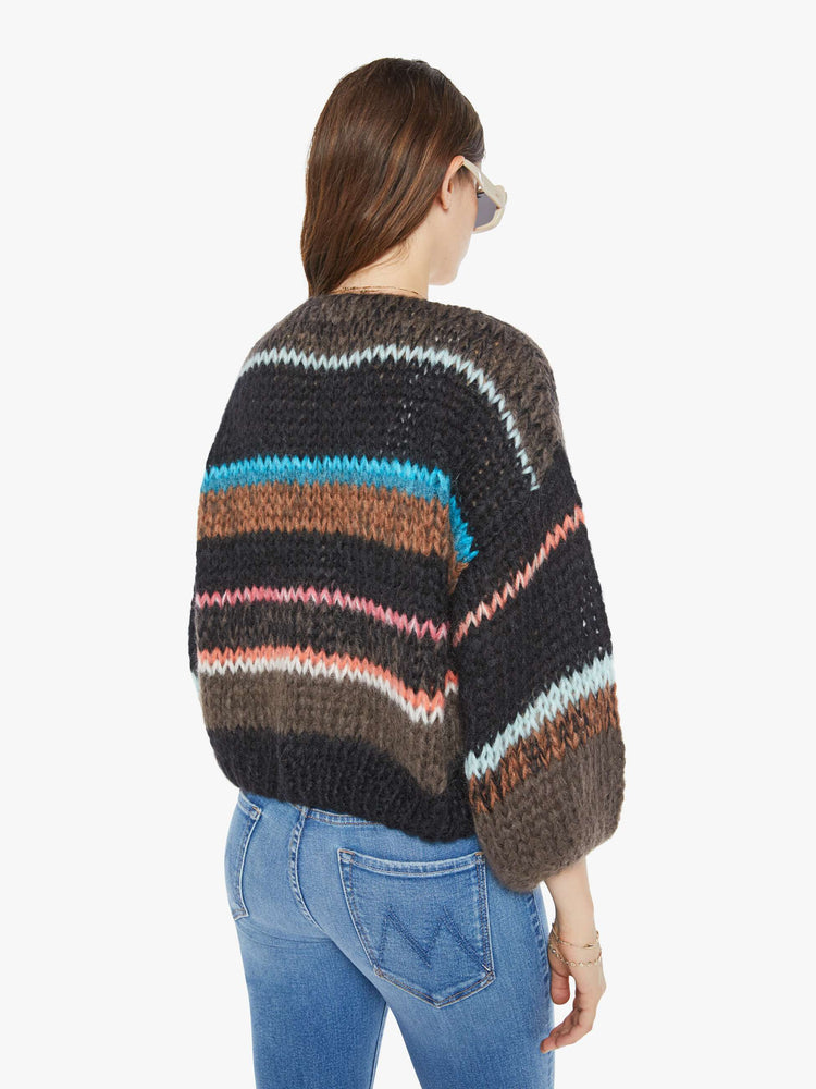 Back view of a woman in a hand knit cardigan with  drop shoulders and bracelet-length balloon sleeves in colorful horizontal stripes.