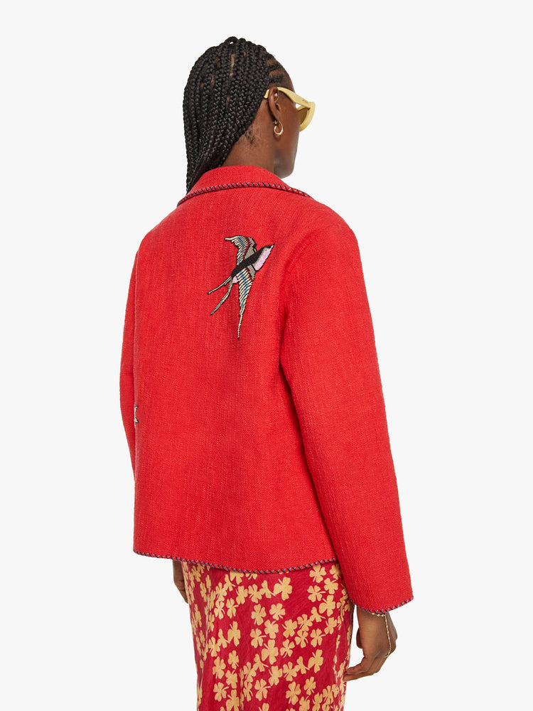 Back view of a woman in a red jacket with beaded motifs and dropped shoulders, front patch pockets and a tailored fit that hugs the body like a blazer.