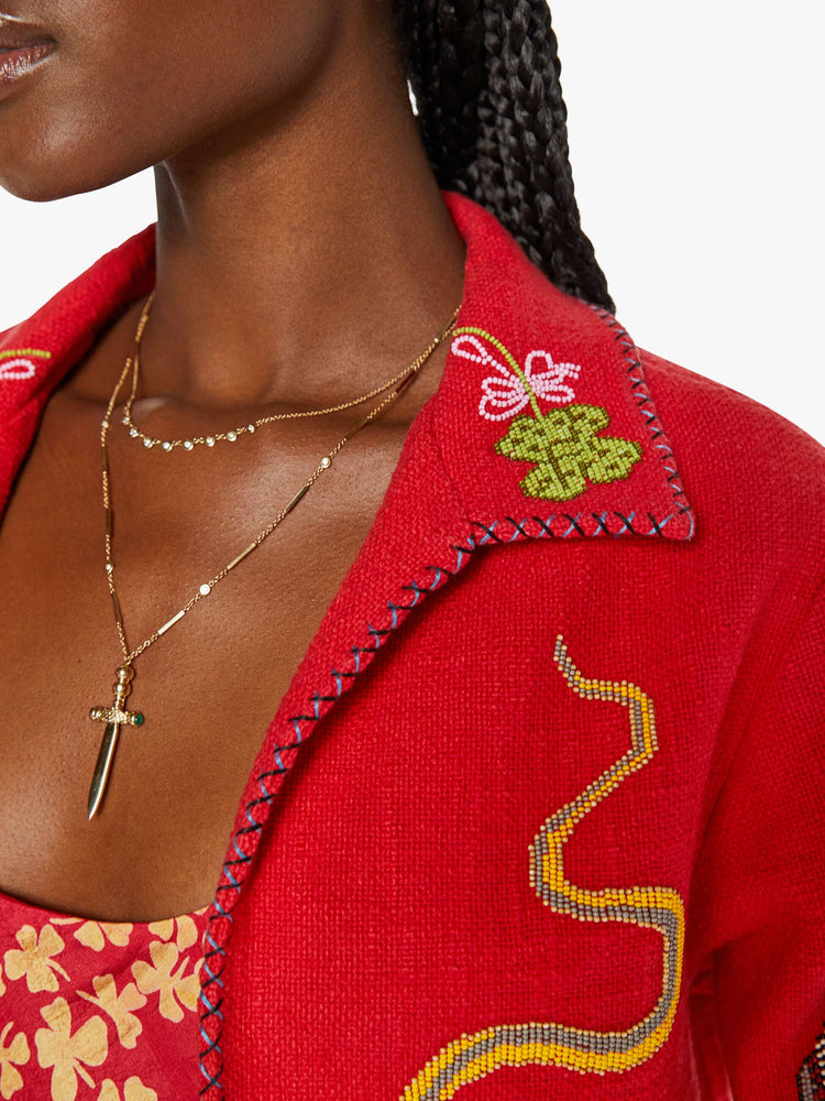 Close up view of a woman in a red jacket with beaded motifs and dropped shoulders, front patch pockets and a tailored fit that hugs the body like a blazer.