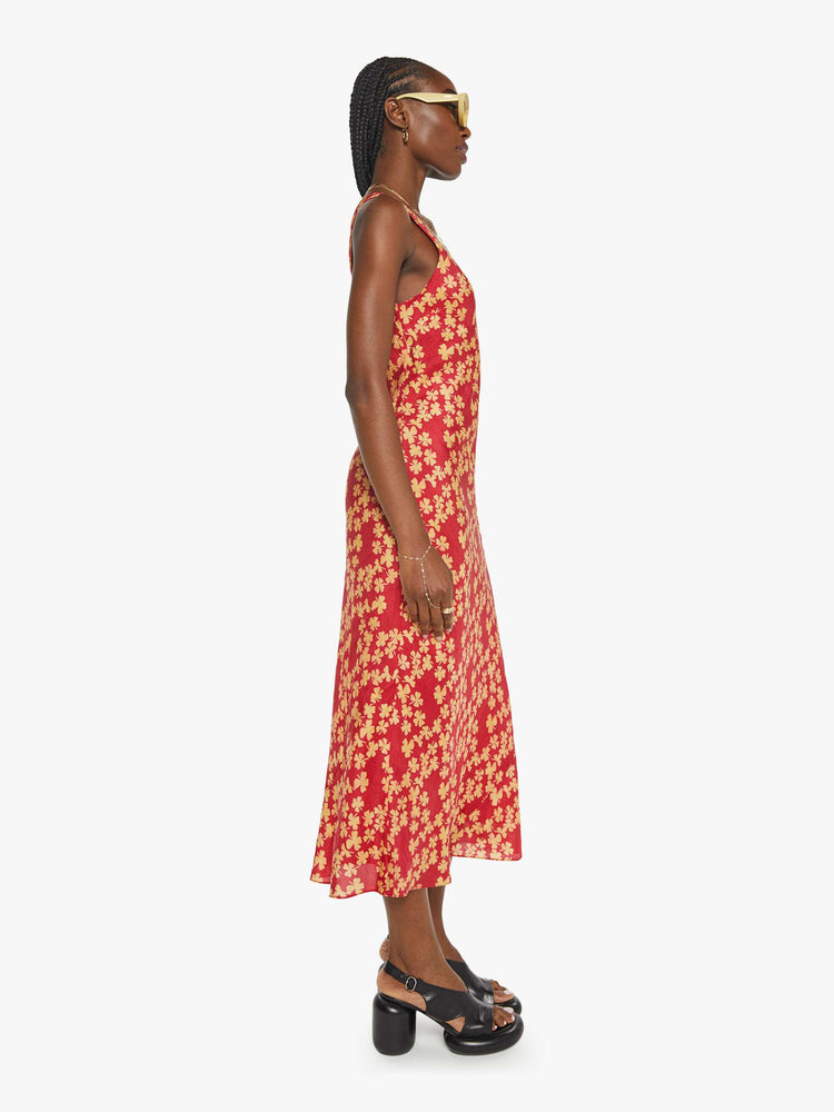 Side view of a woman in a silk red dress with cream clovers, and features a scoop neck, narrow fit and an ankle-length hem.