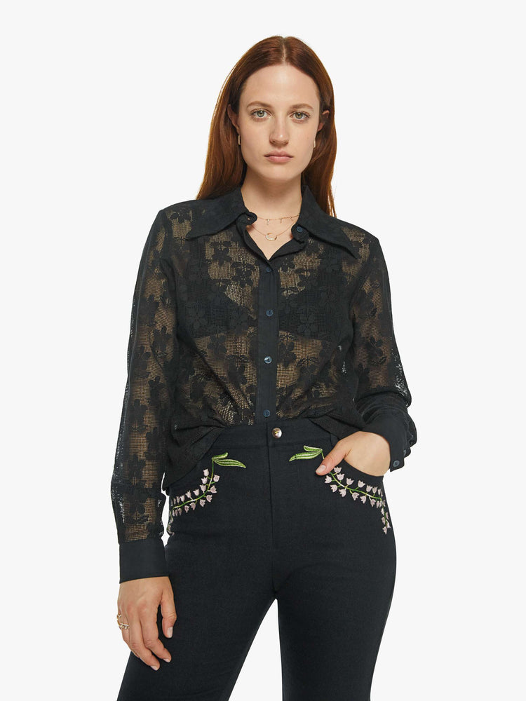 Front view of a woman in semi sheer black shirt with a daisy pattern, and features extra-long sleeves and a loose fit.