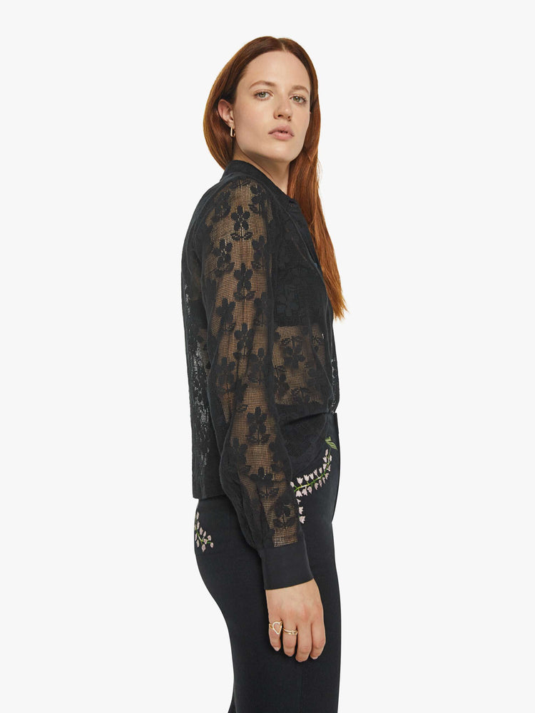 Side view of a woman in semi sheer black shirt with a daisy pattern, and features extra-long sleeves and a loose fit.