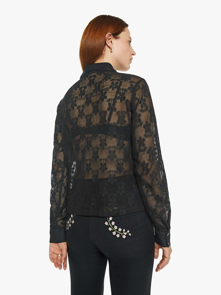 Back view of a woman in semi sheer black shirt with a daisy pattern, and features extra-long sleeves and a loose fit.