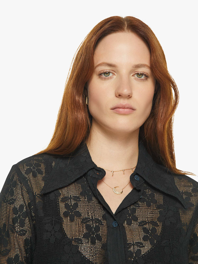 Close up view of a woman in semi sheer black shirt with a daisy pattern, and features extra-long sleeves and a loose fit.