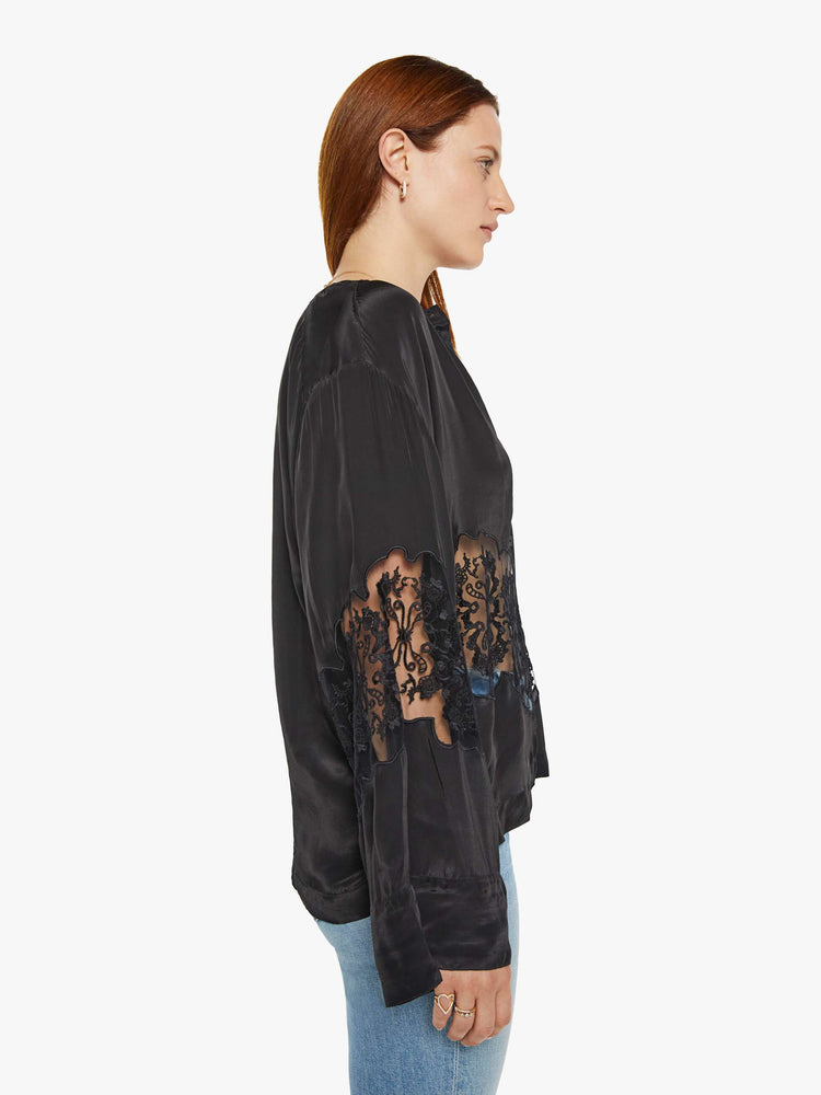 Side view of a woman in a black with lace details at the waist and sleeves blouse with long loose sleeves, a flowy fit and buttons down the front.