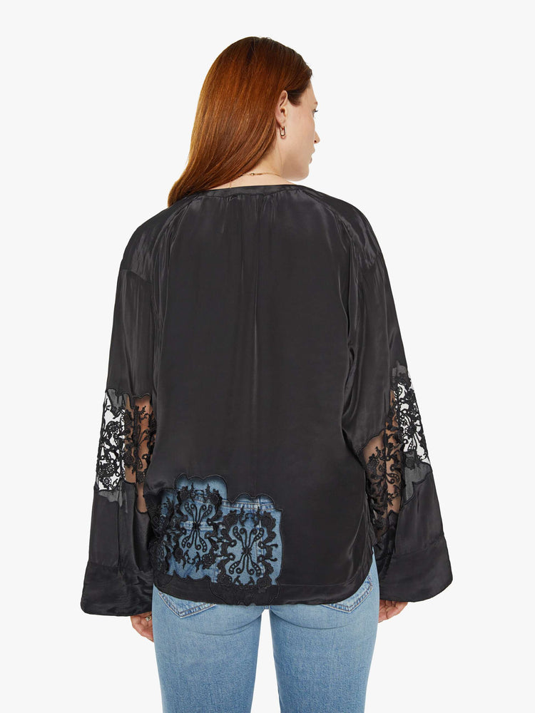 Back view of a woman in a black with lace details at the waist and sleeves blouse with long loose sleeves, a flowy fit and buttons down the front.