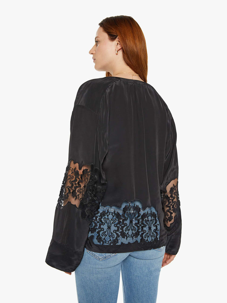 Back view of a woman in a black with lace details at the waist and sleeves blouse with long loose sleeves, a flowy fit and buttons down the front.