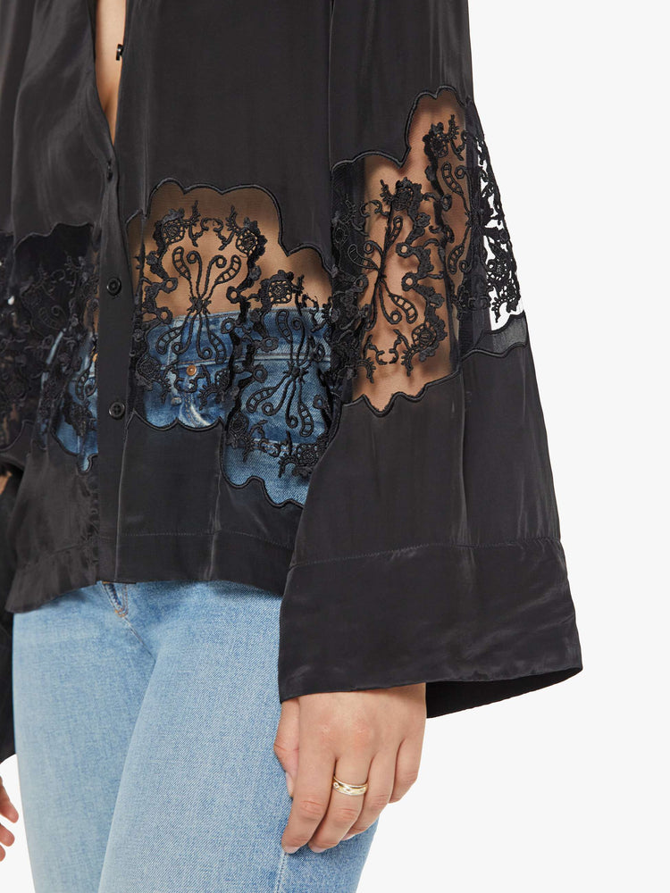 Detailed view of a woman in a black with lace details at the waist and sleeves blouse with long loose sleeves, a flowy fit and buttons down the front.