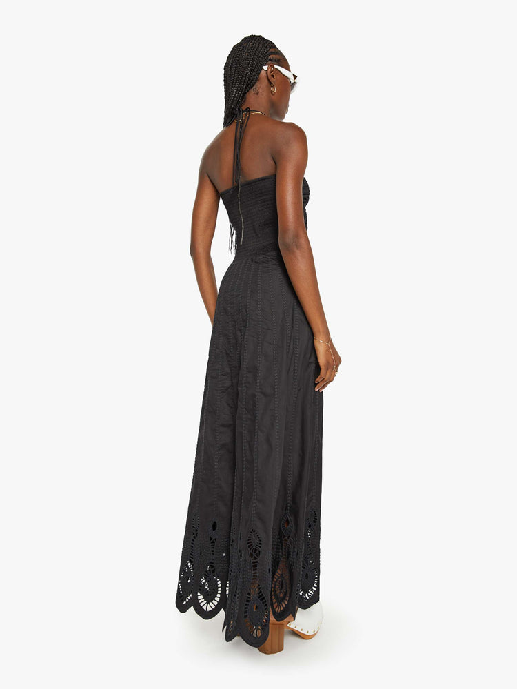 Back view of a woman in a black maxi dress a halter neck, gathered bodice and a floor-length hem with eyelet details.