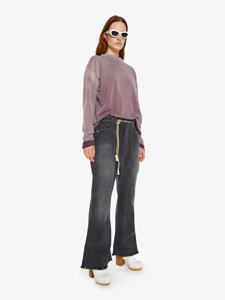 Side angle view of a woman faded black pants have a mid rise, flared leg, belted waistband and a loose fit.