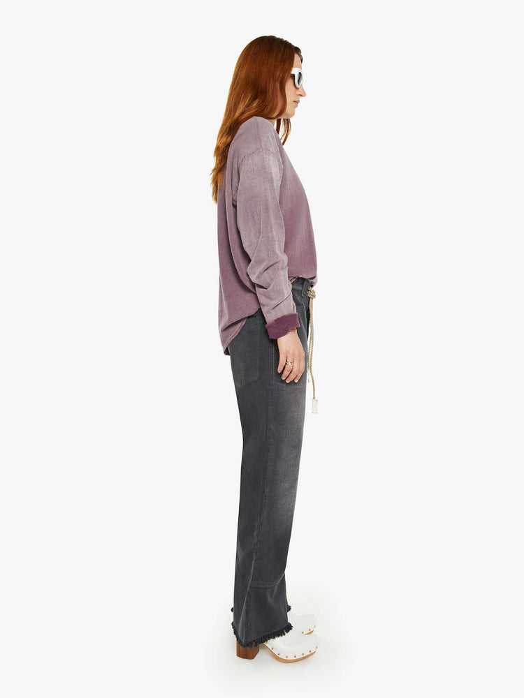 Side view of a woman faded black pants have a mid rise, flared leg, belted waistband and a loose fit.