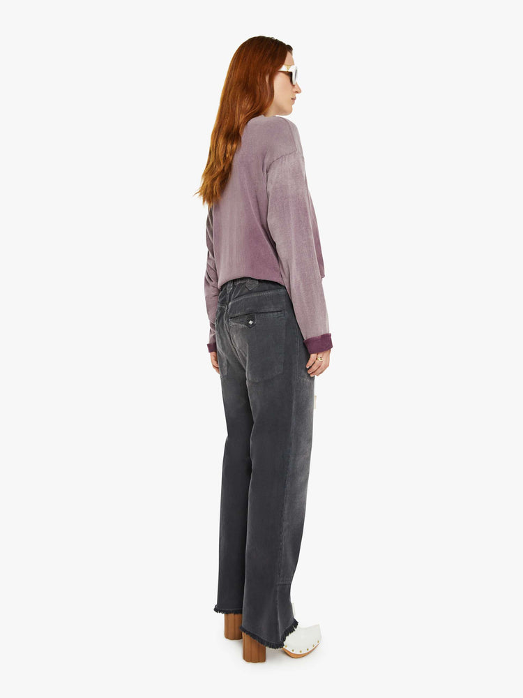 Back view of a woman faded black pants have a mid rise, flared leg, belted waistband and a loose fit.