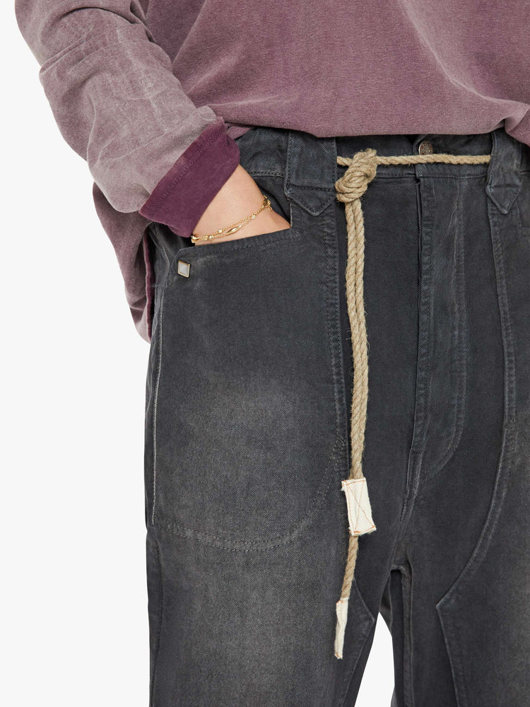 Close up pocket view of a woman faded black pants have a mid rise, flared leg, belted waistband and a loose fit.