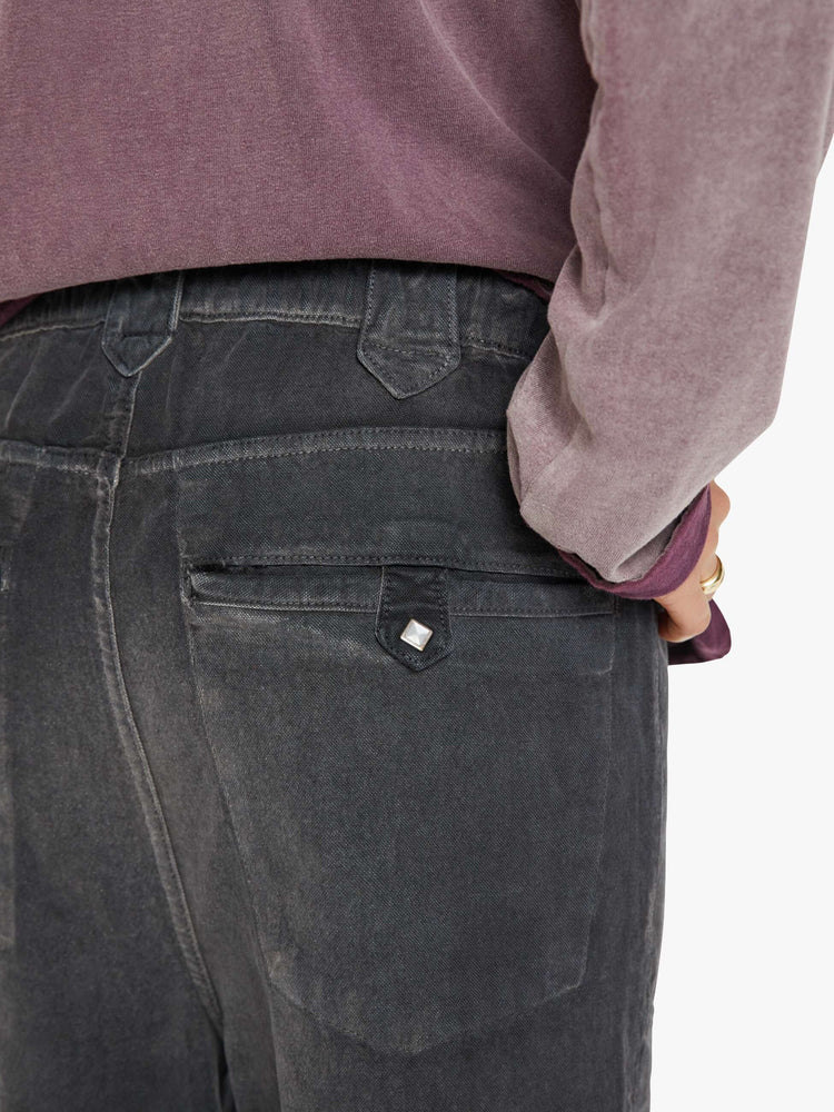 Close up back pocket view of a woman faded black pants have a mid rise, flared leg, belted waistband and a loose fit.