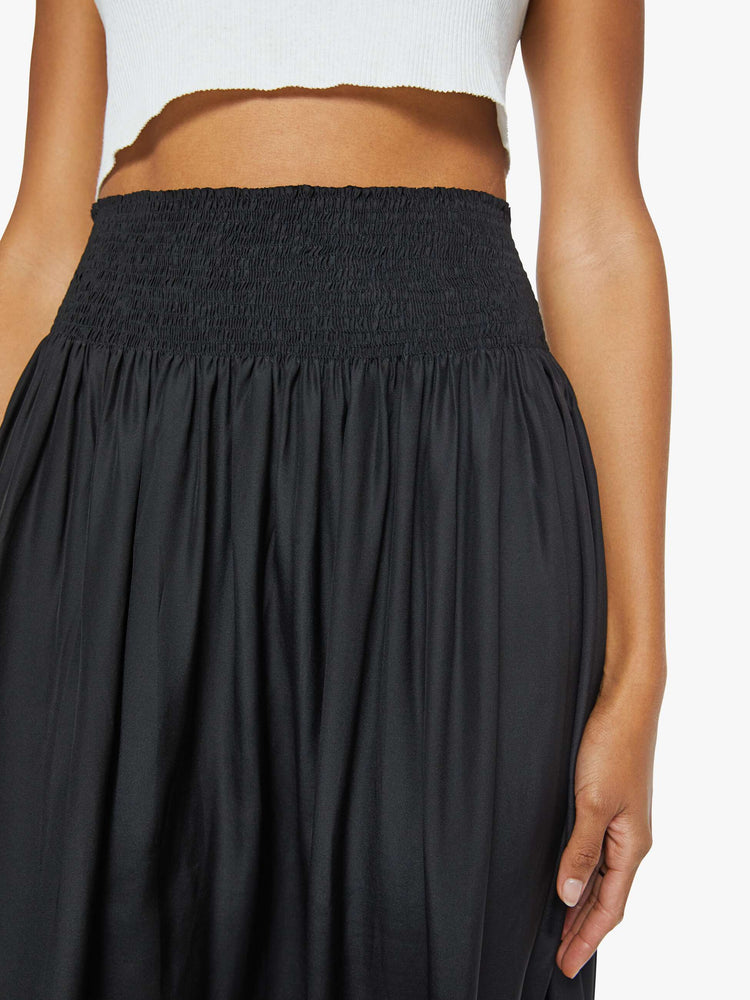 Front close up  view of a woman wearing a black skirt featuring a wide elastic waistband and a flowy fit, paired with a cropped white tank top.