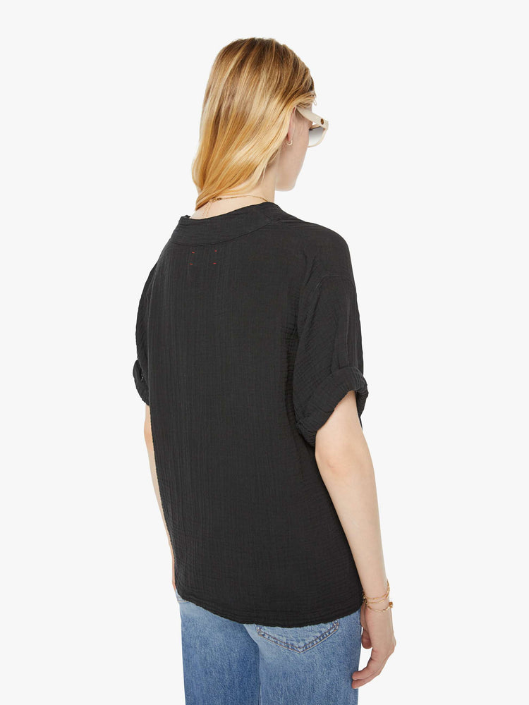 Back view of a woman wearing a black top featuring a deep v-neck, rolled sleeves, and a boxy fit.